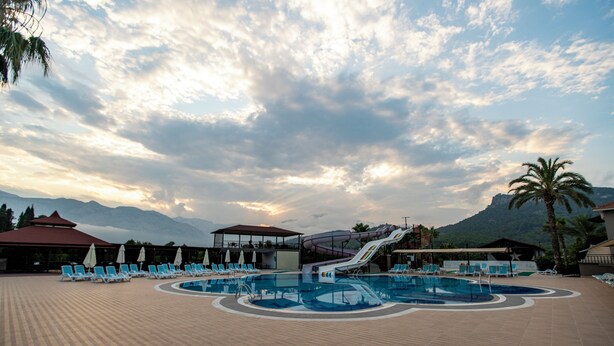 A resort pool area with lounge chairs, a water slide, and a mountain backdrop.