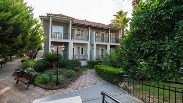 Un edificio residencial de varios pisos con balcones, un patio empedrado y vegetación circundante.