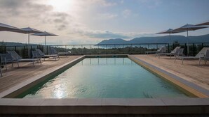 Piscina rectangular con muelle de madera, rodeada de sillones y sombrillas, con vistas a un paisaje montañoso.