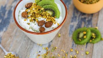 A bowl of yogurt topped with kiwi slices, almonds, and chopped nuts on a wooden surface.