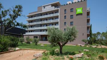 Um hotel com vários andares, varandas, um jardim com pedras e plantas, e uma placa com a inscrição 'ibis Styles'.