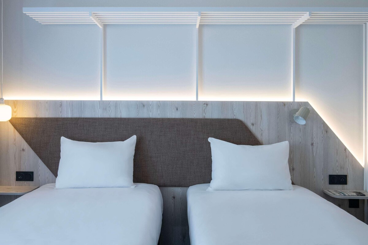 A hotel room with two beds, a wooden headboard, and a wall-mounted light fixture.
