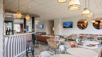 A modern restaurant interior with round tables, bar area, and hanging pendant lights.