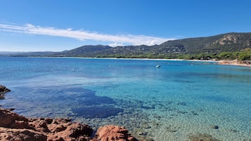 A coastal landscape with clear blue waters, rocky shoreline, and distant hills.