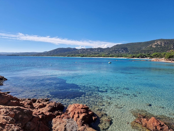 Un paisaje costero con aguas azules cristalinas, costa rocosa y colinas al fondo.