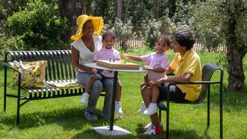 A group of people sitting on a bench in a park with a table in front of them.