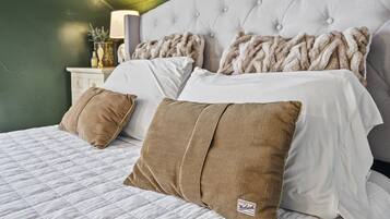 Un dormitorio con cabecera capitonada, colcha blanca acolchada y dos almohadas marrones.