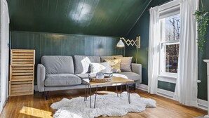 Un salon chaleureux avec un canapé gris, des caisses en bois, un tapis en fausse fourrure blanche et une fenêtre agrémentée de rideaux blancs.
