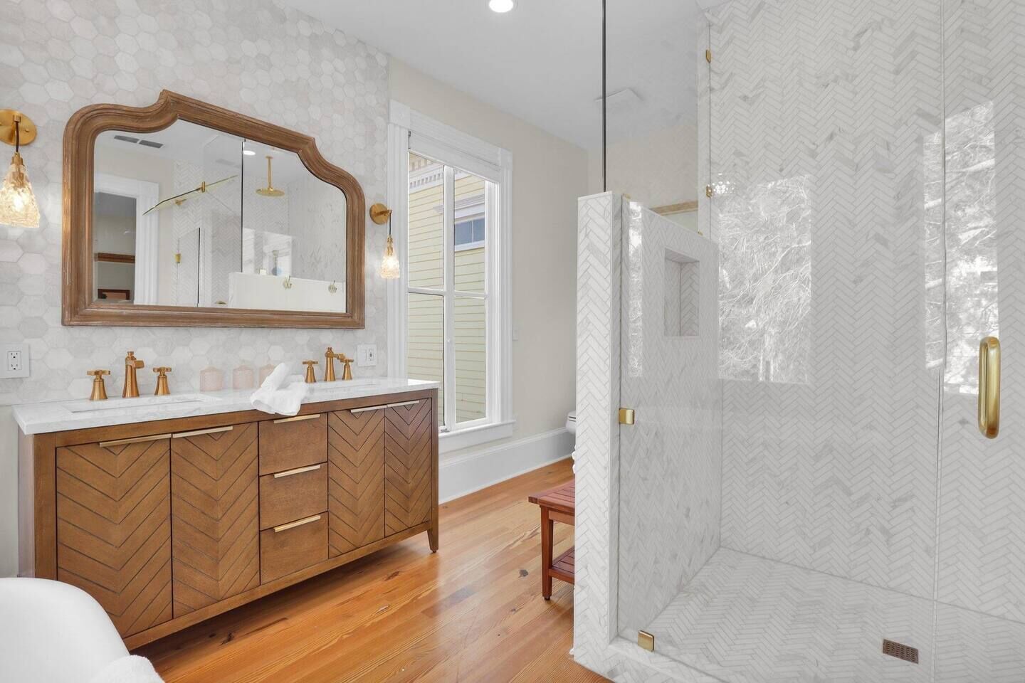 Une salle de bain moderne avec un meuble-lavabo en bois, un grand miroir et une paroi de douche à motifs en chevrons.
