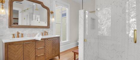 Une salle de bain moderne avec un meuble-lavabo en bois, un grand miroir et une paroi de douche à motifs en chevrons.