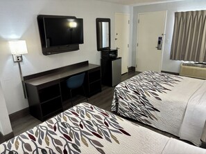 Ett hotellrum med TV, skrivbord, stol, två sängar med sängkläder med ett lövmönster och en spegel.
