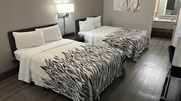 A hotel room with two beds, a nightstand, a lamp, a mirror, and a painting on the wall.