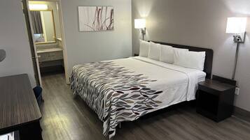 A hotel room with a bed, bedside tables, a nightstand, a wall-mounted lamp, and a door leading to a bathroom.
