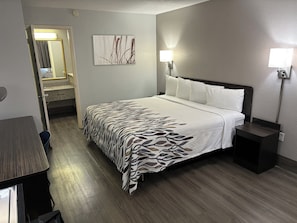 A hotel room with a bed, bedside tables, a nightstand, a wall-mounted lamp, and a door leading to a bathroom. - Red Roof Inn Birmingham – Highway 280 (Birmingham)