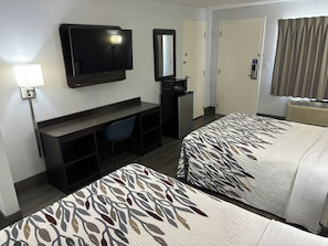 A hotel room with a TV, desk, chair, two beds with leaf-patterned bedding, and a microwave.