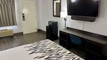 Habitación de hotel con cama, televisión, escritorio, silla, lámpara de escritorio y ventana con cortinas.