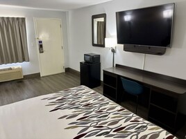 Habitación de hotel con cama, televisión, escritorio, silla, lámpara de escritorio y ventana con cortinas.