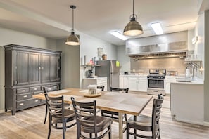 A modern kitchen with a large dining table, dark cabinetry, and stainless steel appliances.
