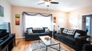 A living room with two dark sofas, a coffee table, a TV, and a ceiling fan.