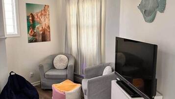 A living room with a flat-screen TV, a grey sofa, a white cabinet, a bean bag, and a patterned rug.