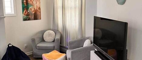 Ein Wohnzimmer mit einem Flachbildfernseher, einem grauen Sofa, einem weißen Schrank, einem Sitzsack und einem gemusterten Teppich.