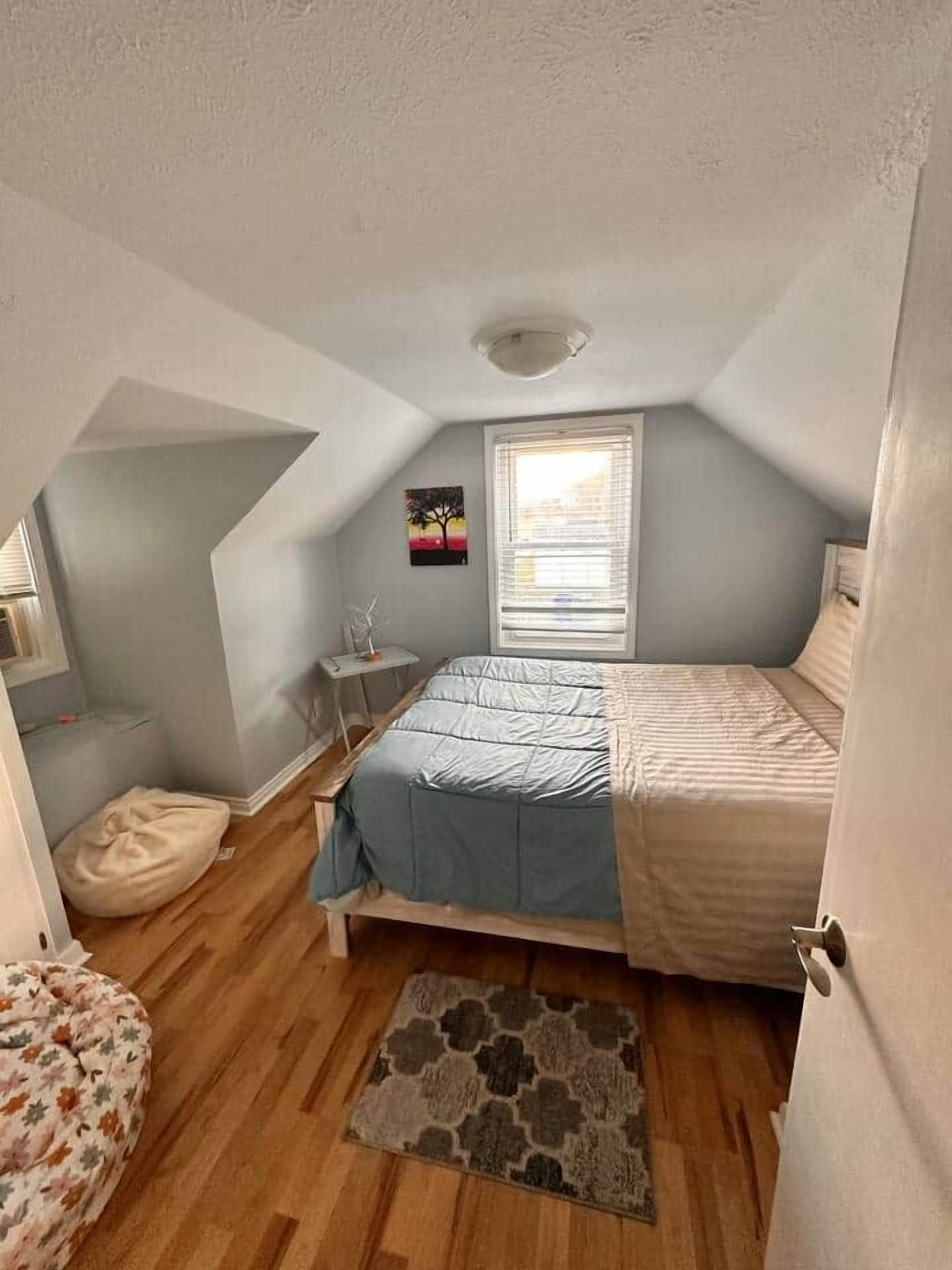 A bedroom with a bed, a window, a small table, and a rug.