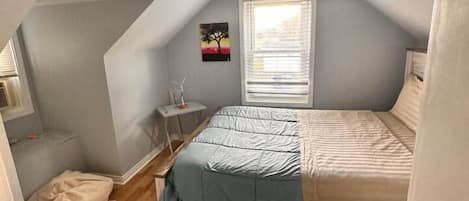 A bedroom with a bed, a window, a small table, and a rug.