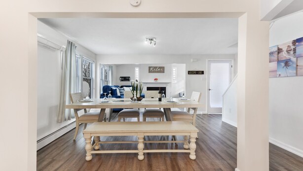 Een eethoek met een houten tafel en bank, een keuken op de achtergrond, en een trap die naar boven leidt.