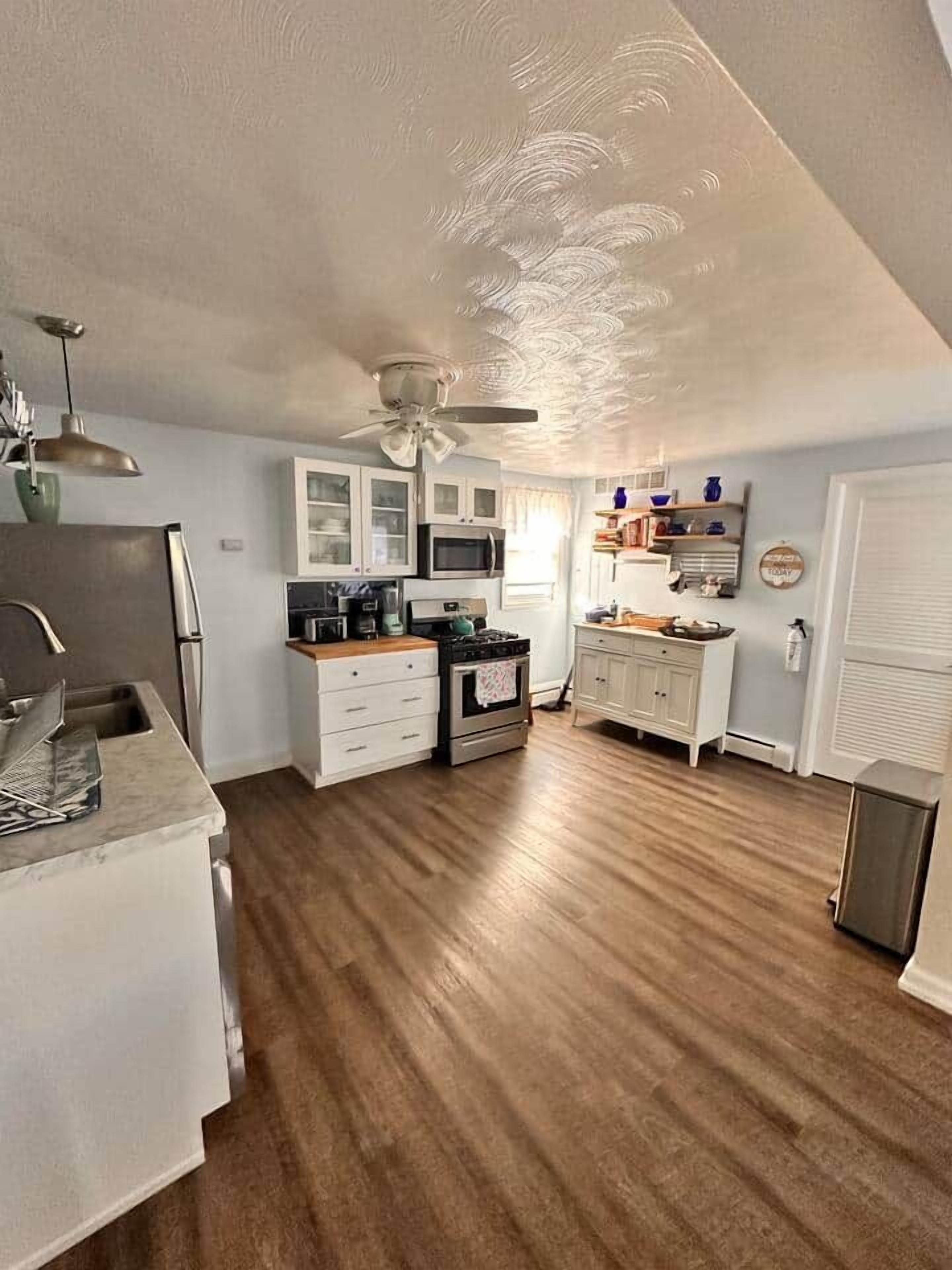 A kitchen with wooden flooring, white cabinetry, a ceiling fan, and a microwave.
