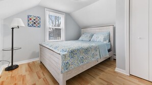 Een slaapkamer met een bed, een raam, een lamp en een plafondlamp.