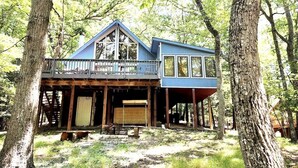 A two-story cabin with a balcony, surrounded by trees. - Cozy A-Frame Cabin • Hot Tub • Game Room • Forest Escape (Hedgesville)
