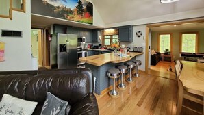 A modern kitchen with a central island, stainless steel appliances, and a dining area with a wooden table and chairs. - Cozy A-Frame Cabin • Hot Tub • Game Room • Forest Escape (Hedgesville)