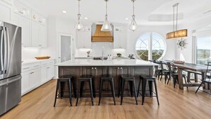 A modern kitchen with white cabinets, a large island with bar stools, and pendant lighting. - Ocean Twelve (Ocean Isle Beach)