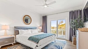 A bedroom with a bed, a bedside table, a lamp, a ceiling fan, a window with curtains, and a view of the outdoors. - Ocean Twelve (Ocean Isle Beach)