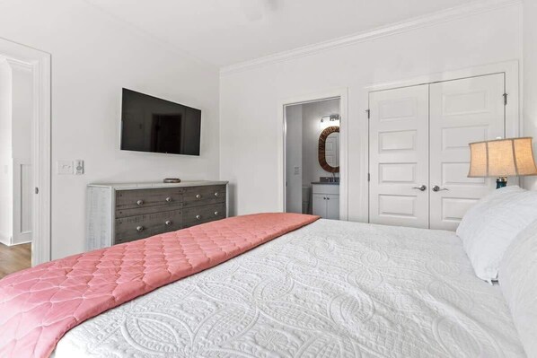 Une chambre à coucher comprenant un lit, une commode, un téléviseur et une porte donnant sur une autre pièce.