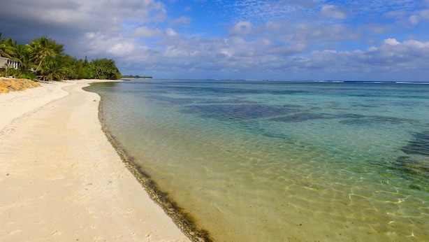 A beach with clear turquoise water, a sandy shore, and a building on the left. - MM Batch South Side (Avavaaroa)