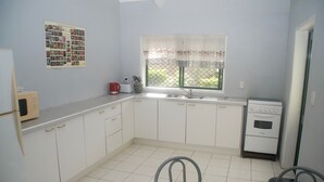 A compact kitchen with white cabinets, a small window with a lace curtain, a microwave, a toaster, and a dishwasher. - MM Batch South Side (Avavaaroa)