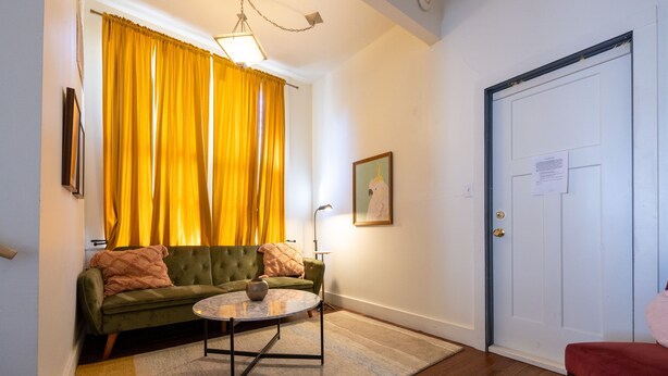 A living room with a green sofa, a round coffee table, and a yellow curtain. - The Downtown Abbey - The Drawing Room (San Marcos)