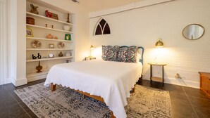 Un dormitorio con cama, mesita de noche, cómoda, estantería y ventana con arco decorativo.
