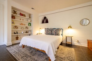 A bedroom with a bed, a nightstand, a dresser, a bookshelf, and a window with a decorative arch. - The Downtown Abbey - The Drawing Room (San Marcos)