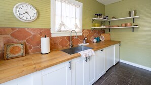 A kitchen with a wooden countertop, white cabinets, a sink, a clock, and shelves with kitchenware. - The Downtown Abbey - The Drawing Room (San Marcos)
