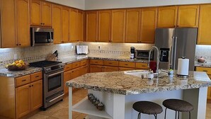 A modern kitchen with wooden cabinets, granite countertops, stainless steel appliances, and a central island with bar stools. - Rancho La Quinta community with amazing pool (La Quinta)