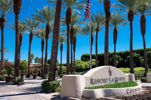 Welcome to Rancho La Quinta Country Club, where manicured landscaping and palm trees frame the entrance.