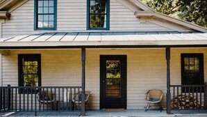 A two-story house with a porch, a black door, and two windows with black frames. - The Starling at Pond Eddy, Cottage (Pond Eddy)