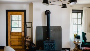 A cozy living room with a wood-burning stove, a glass coffee table, and a green armchair. - The Starling at Pond Eddy, Cottage (Pond Eddy)