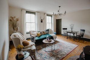 Relax in a spacious living room with a comfortable seating area, dining table for two, and a chandelier.