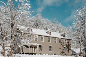 Une maison à deux étages, dont le toit est recouvert de neige, entourée d’arbres.