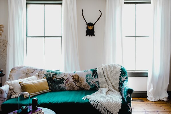 Une pièce avec un canapé vert, un plaid blanc et une branche de cerf décorative accrochée au mur.