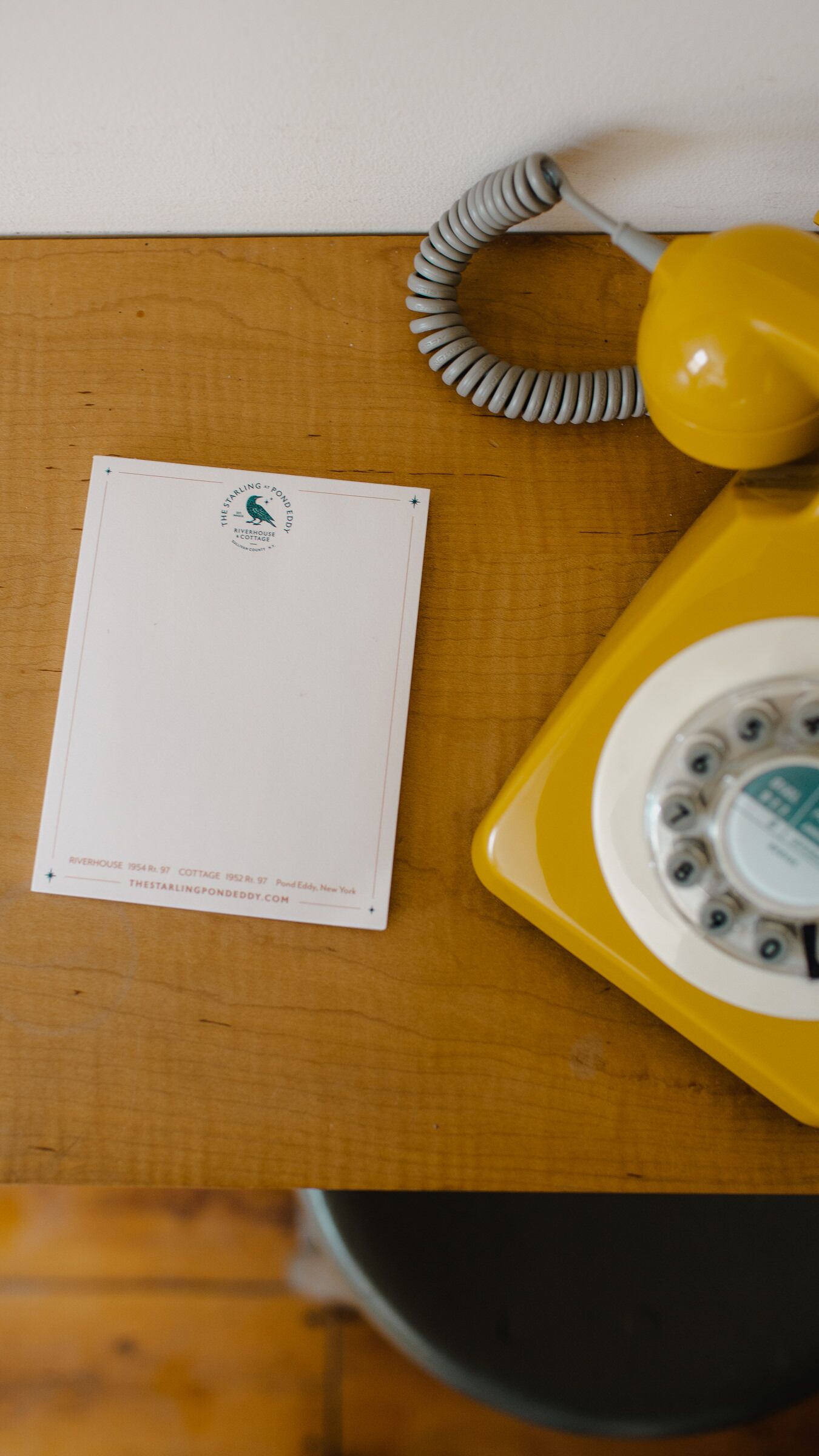A yellow rotary phone and a white postcard on a wooden surface.