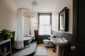 Une salle de bain équipée d’une baignoire, de toilettes, d’un lavabo et d’une fenêtre avec des rideaux.